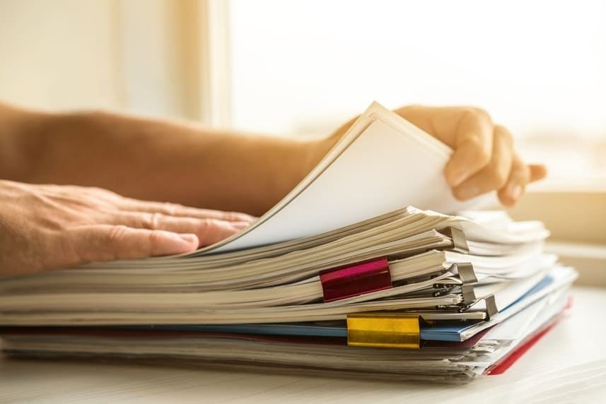 Mãos folheando uma pilha de documentos técnicos sobre a mesa